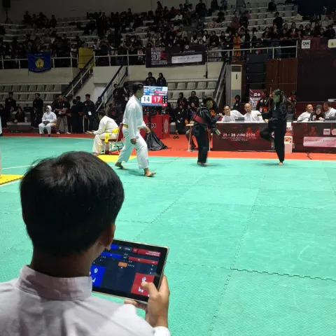 Suasana pertandingan Kejuaraan Pencak Silat CNN Indonesia 2 Piala Presiden di Padepokan Pencak Silat TMII, Jakarta Timur, dengan pesilat bertanding di atas gelanggang dan papan skor digital terlihat di arena.