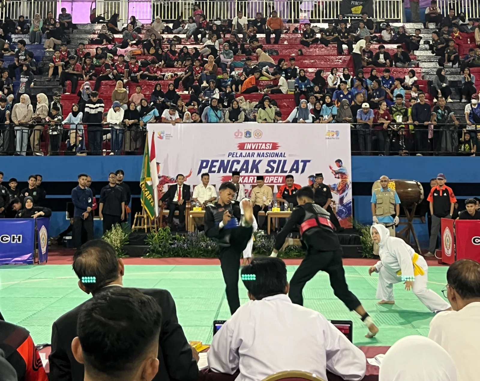 Dua pesilat remaja bertanding di hadapan wasit dengan tribun GOR Ciracas yang dipenuhi penonton dalam Invitasi Pelajar Nasional Pencak Silat Jakarta Open 2026.